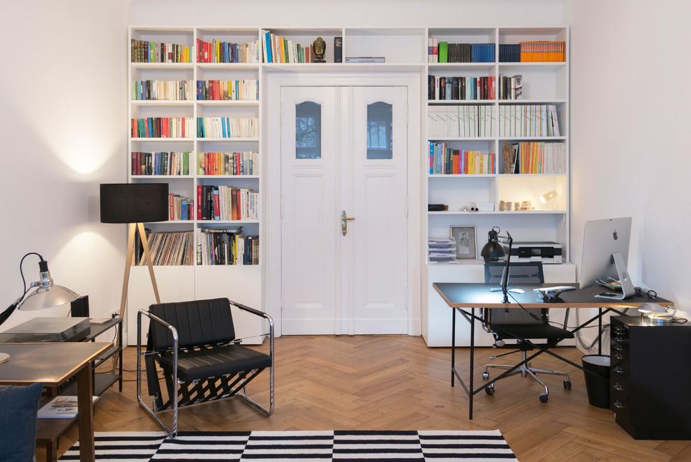 Photo of an expansive contemporary home office in Berlin with white walls, medium hardwood floors, beige floor, a library, no fireplace and a freestanding desk.
