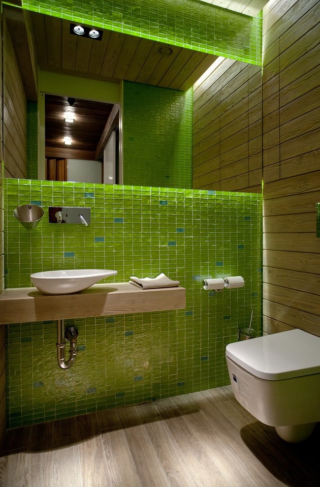 Small contemporary powder room in Saint Petersburg with a wall-mount toilet, green tile, mosaic tile, a vessel sink, light hardwood floors, wood benchtops, beige floor and beige benchtops.