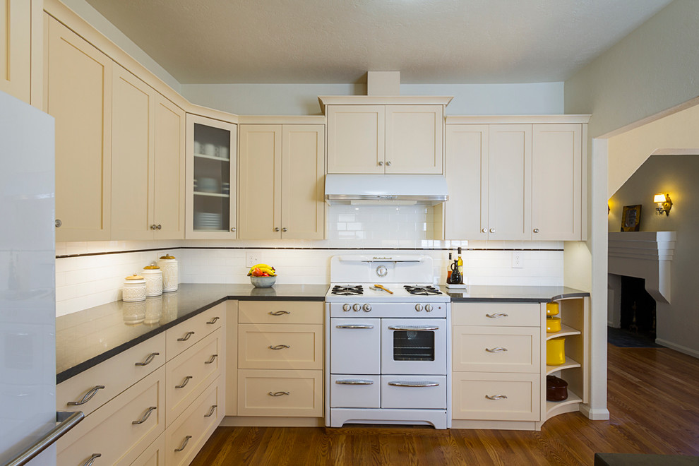 This is an example of a mid-sized country l-shaped eat-in kitchen in Phoenix with a farmhouse sink, shaker cabinets, yellow cabinets, quartz benchtops, white splashback, subway tile splashback, white appliances, medium hardwood floors, no island and brown floor.