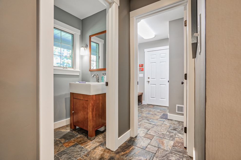 This is an example of a mid-sized transitional powder room in Detroit with flat-panel cabinets, brown cabinets, a two-piece toilet, grey walls, slate floors, an integrated sink, brown floor and white benchtops.
