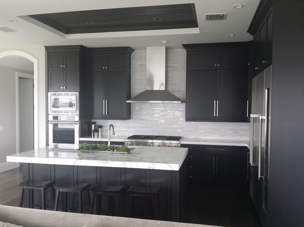 This is an example of a mid-sized traditional l-shaped open plan kitchen in Miami with an undermount sink, shaker cabinets, black cabinets, marble benchtops, white splashback, matchstick tile splashback, stainless steel appliances, dark hardwood floors and with island.