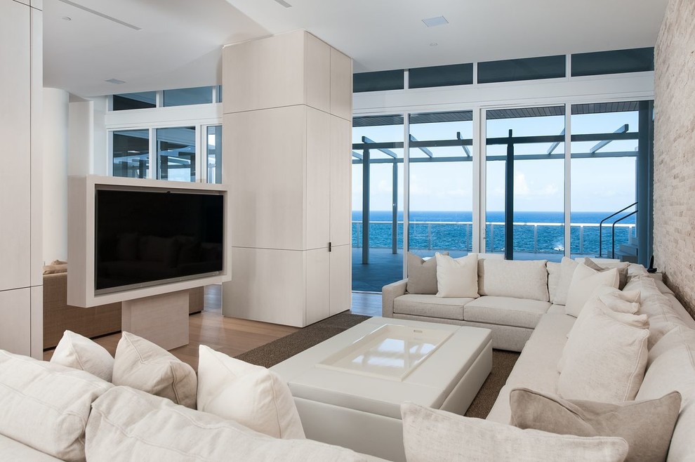 This is an example of a mid-sized contemporary formal enclosed living room in Miami with beige walls, light hardwood floors, a freestanding tv and brown floor.