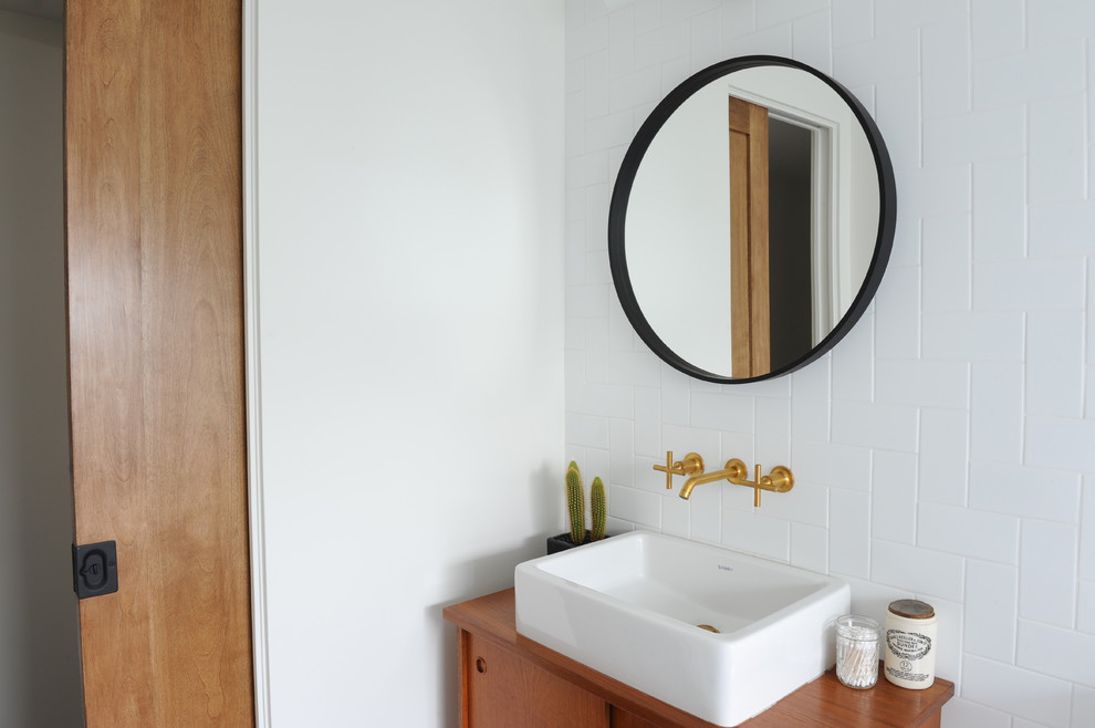 Small midcentury 3/4 bathroom in Vancouver with flat-panel cabinets, medium wood cabinets, an alcove tub, a shower/bathtub combo, a two-piece toilet, white tile, ceramic tile, white walls, porcelain floors, a vessel sink, wood benchtops, white floor and a shower curtain.