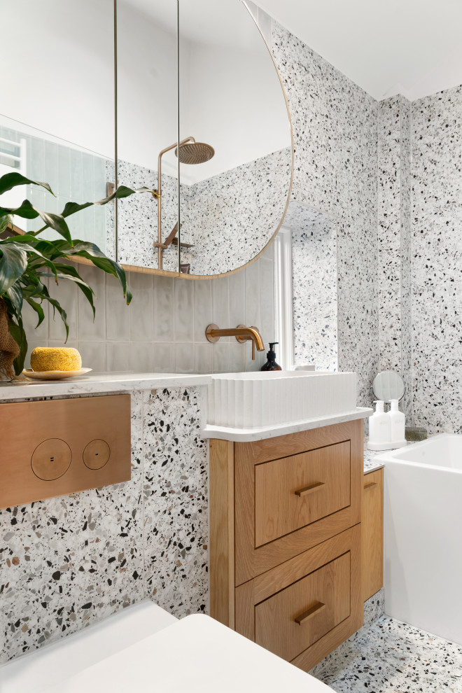 Photo of a small contemporary master bathroom in Melbourne with shaker cabinets, medium wood cabinets, a drop-in tub, a shower/bathtub combo, a one-piece toilet, multi-coloured tile, porcelain tile, multi-coloured walls, terrazzo floors, a vessel sink, engineered quartz benchtops, multi-coloured floor, a hinged shower door, white benchtops, a single vanity, a built-in vanity, vaulted and planked wall panelling.