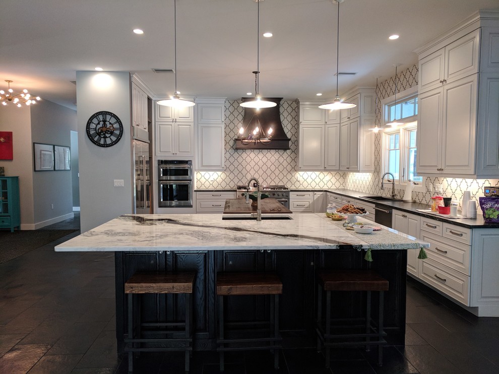 Expansive transitional u-shaped open plan kitchen in DC Metro with an integrated sink, raised-panel cabinets, white cabinets, granite benchtops, white splashback, stainless steel appliances, with island, black floor and multi-coloured benchtop.