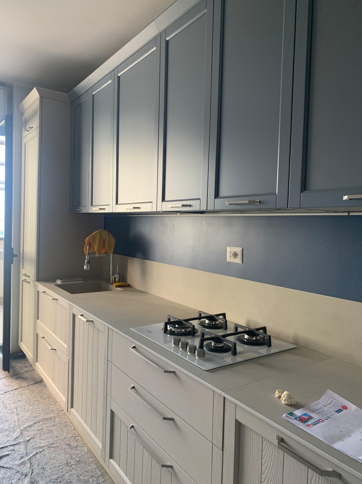 Immagine di una cucina parallela design chiusa e di medie dimensioni con lavello da incasso, ante con riquadro incassato, ante blu, top in granito, paraspruzzi beige, paraspruzzi in granito, elettrodomestici bianchi, pavimento in cemento, pavimento grigio e top beige