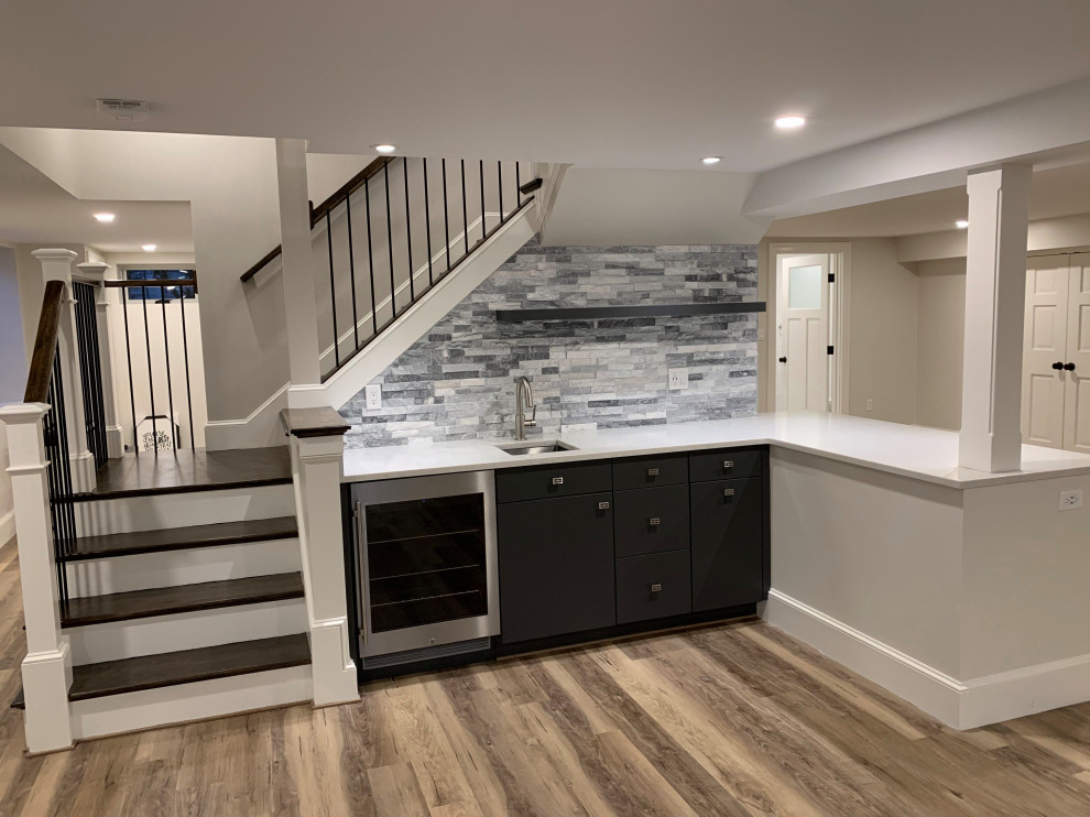 Photo of a mid-sized transitional l-shaped wet bar in Boston with an undermount sink, grey cabinets, solid surface benchtops, grey splashback, stone tile splashback, medium hardwood floors, brown floor and white benchtop.