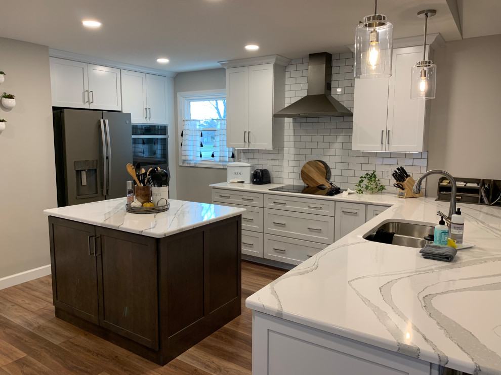 Inspiration for a large transitional u-shaped vinyl floor and brown floor open concept kitchen remodel with an undermount sink, shaker cabinets, white cabinets, quartz countertops, white backsplash, ceramic backsplash, stainless steel appliances, an island and white countertops