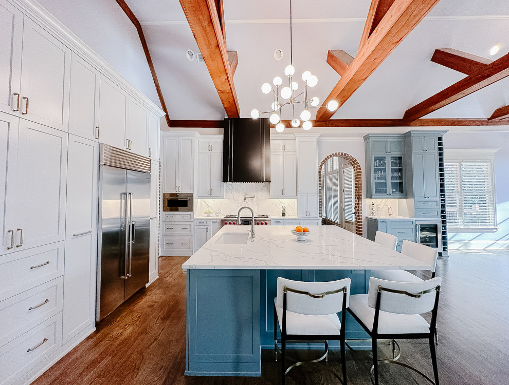 Example of a huge transitional l-shaped medium tone wood floor, brown floor and exposed beam open concept kitchen design in Atlanta with a single-bowl sink, shaker cabinets, white cabinets, quartz countertops, white backsplash, quartz backsplash, stainless steel appliances, an island and white countertops