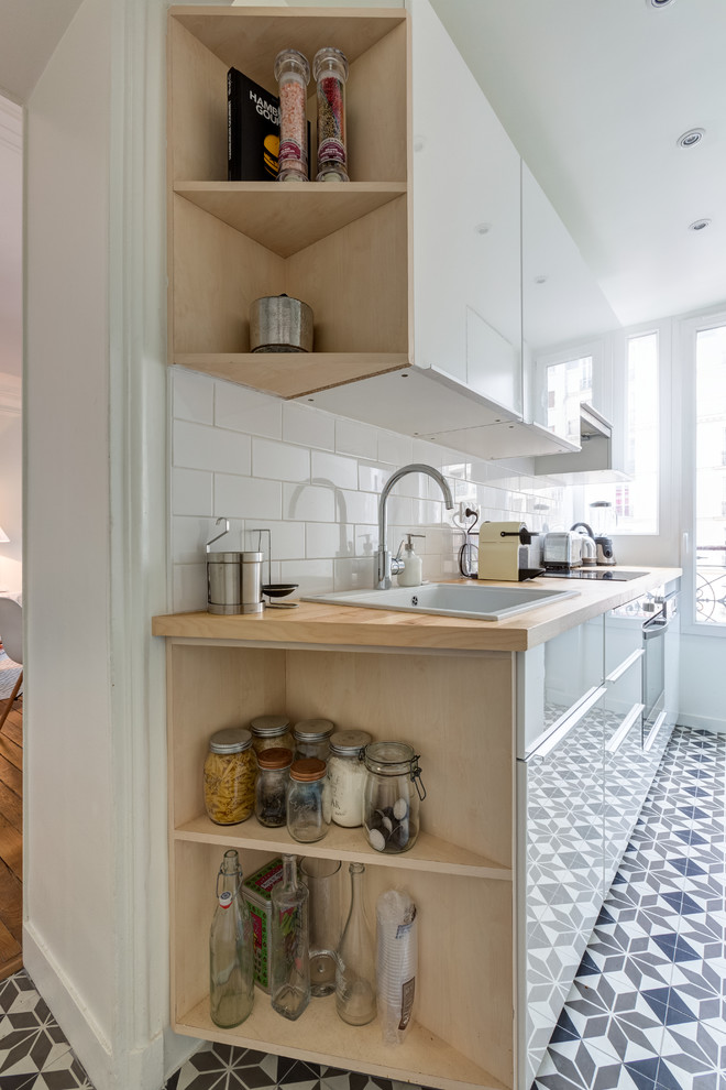 This is an example of a small scandinavian l-shaped separate kitchen in Paris with a drop-in sink, flat-panel cabinets, white cabinets, wood benchtops, white splashback, porcelain splashback, stainless steel appliances, cement tiles, no island, multi-coloured floor and beige benchtop.