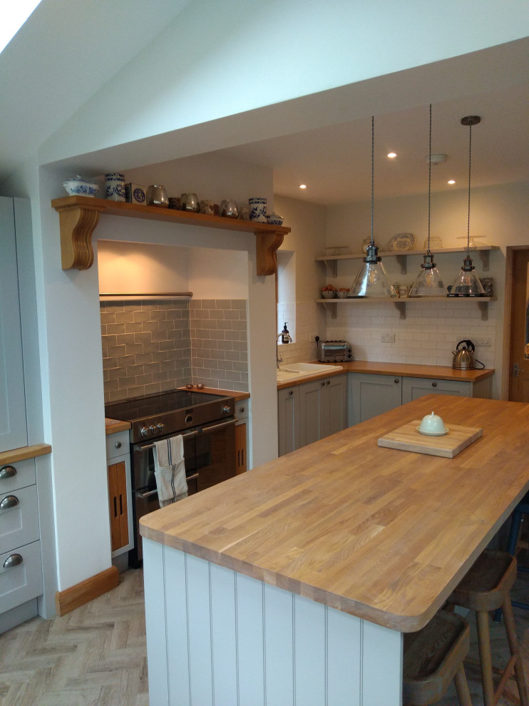 Inspiration for a mid-sized traditional l-shaped open plan kitchen in Cambridgeshire with shaker cabinets, grey cabinets, wood benchtops, white splashback, subway tile splashback and with island.