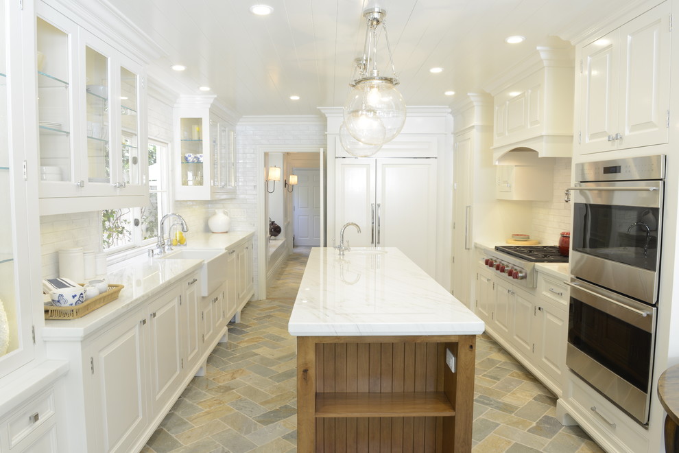 This is an example of a traditional kitchen in Los Angeles with a farmhouse sink, raised-panel cabinets, white cabinets, white splashback, subway tile splashback, stainless steel appliances and with island.
