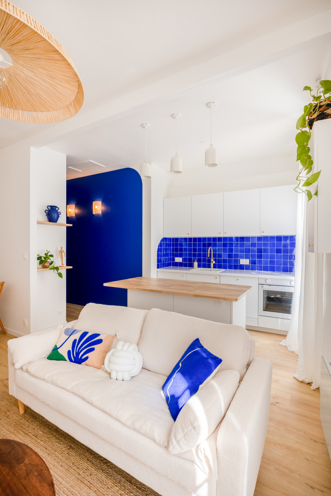 Inspiration for a mid-sized beach style single-wall open plan kitchen in Other with an undermount sink, beaded inset cabinets, white cabinets, blue splashback, coloured appliances, light hardwood floors, with island and white benchtop.