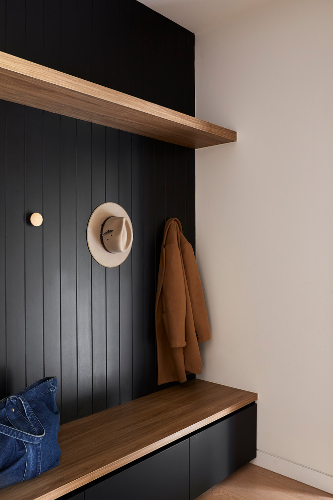 Cette image montre une petite entrée minimaliste avec un vestiaire, un mur noir et parquet clair.