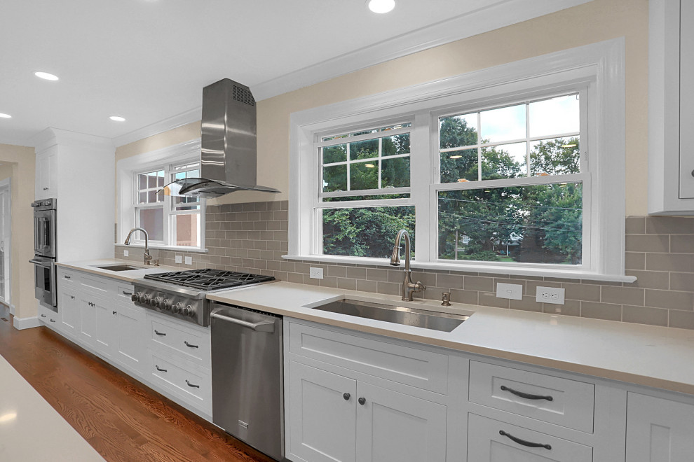 Inspiration for a large transitional medium tone wood floor kitchen remodel with an undermount sink, recessed-panel cabinets, white cabinets, quartzite countertops, gray backsplash, subway tile backsplash, stainless steel appliances, two islands and white countertops