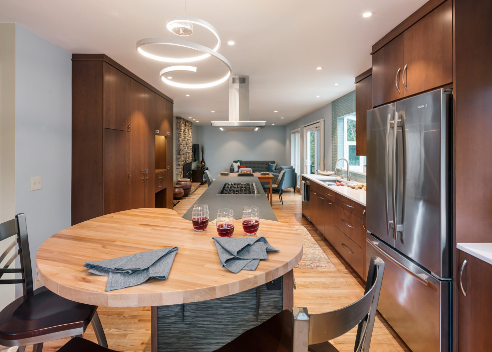 This is an example of a mid-sized contemporary galley eat-in kitchen in Portland with an undermount sink, flat-panel cabinets, dark wood cabinets, quartz benchtops, blue splashback, glass tile splashback, stainless steel appliances, medium hardwood floors, with island, brown floor and multi-coloured benchtop.