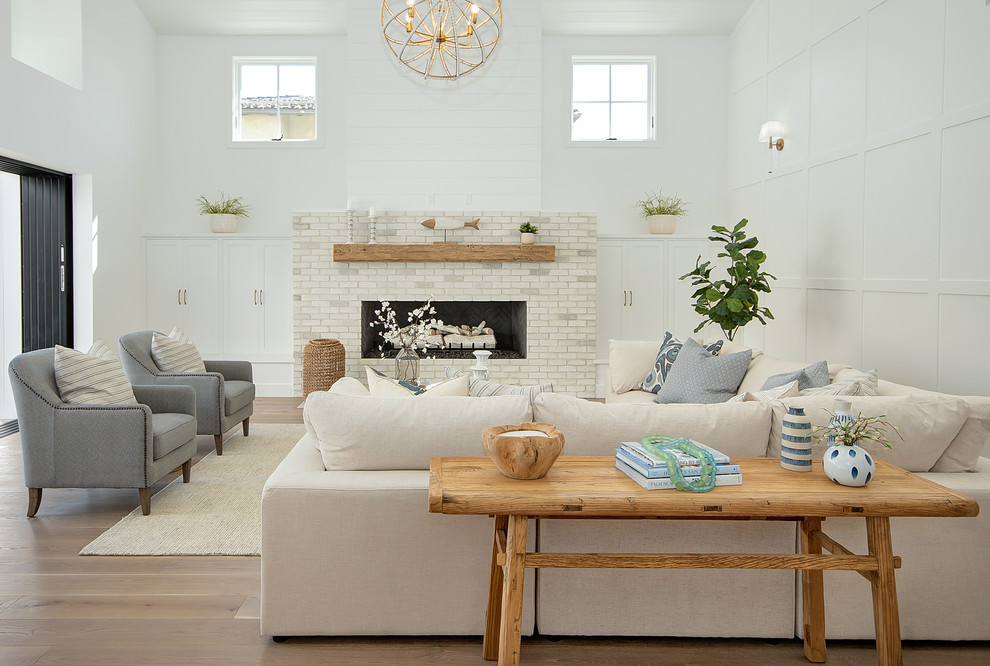 Design ideas for a beach style formal open concept living room in Orange County with white walls, medium hardwood floors, a standard fireplace, a brick fireplace surround, no tv and brown floor.