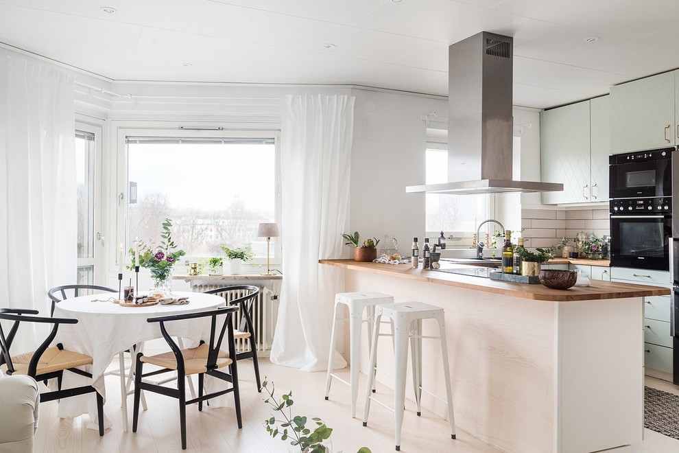 Inspiration for a scandinavian u-shaped eat-in kitchen in Gothenburg with flat-panel cabinets, green cabinets, wood benchtops, white splashback, black appliances, painted wood floors, a peninsula and white floor.