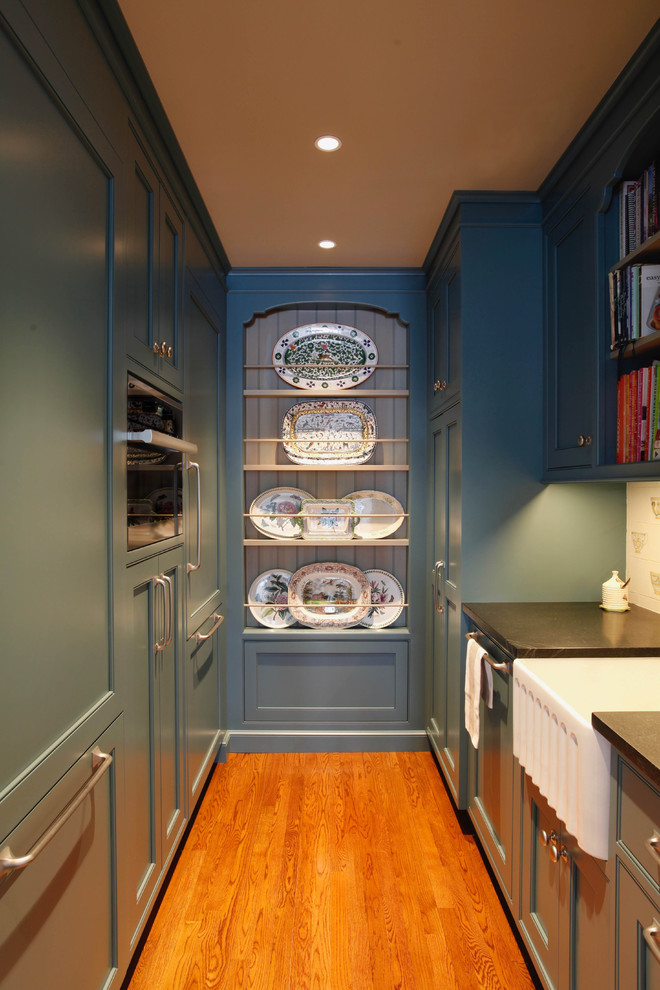 Inspiration for a large traditional galley kitchen pantry in Bridgeport with a farmhouse sink, beaded inset cabinets, white cabinets, soapstone benchtops, green splashback, porcelain splashback, medium hardwood floors, with island, brown floor, black benchtop and panelled appliances.