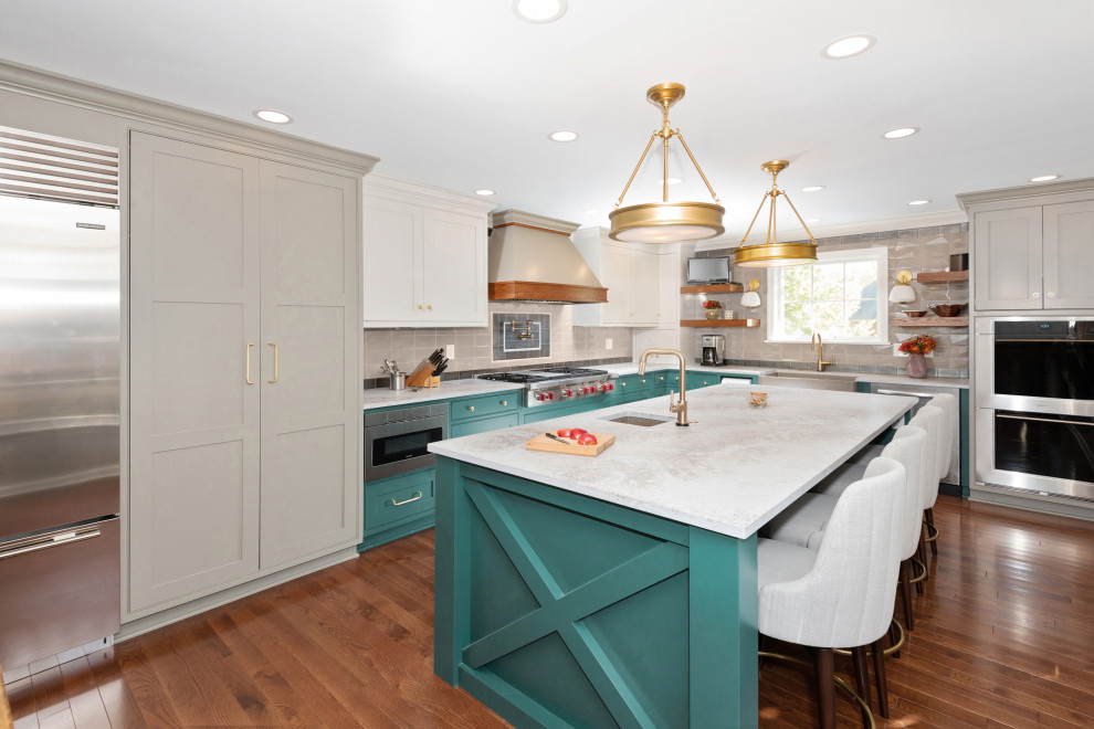 Example of a large transitional l-shaped light wood floor and brown floor kitchen pantry design with a farmhouse sink, beaded inset cabinets, green cabinets, quartz countertops, beige backsplash, subway tile backsplash, stainless steel appliances, an island and gray countertops
