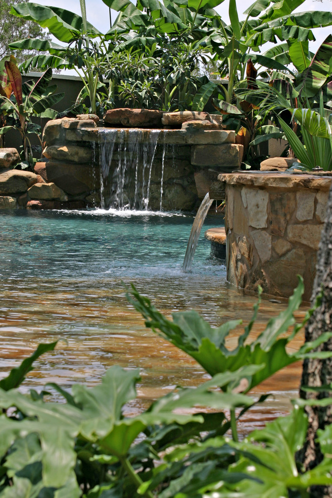 This is an example of a mid-sized tropical backyard custom-shaped natural pool in Austin with natural stone pavers and a hot tub.