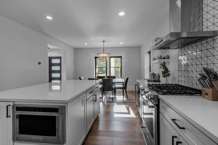 Eat-in kitchen - mid-sized transitional l-shaped light wood floor and brown floor eat-in kitchen idea with an undermount sink, shaker cabinets, white cabinets, quartz countertops, white backsplash, ceramic backsplash, stainless steel appliances, an island and white countertops