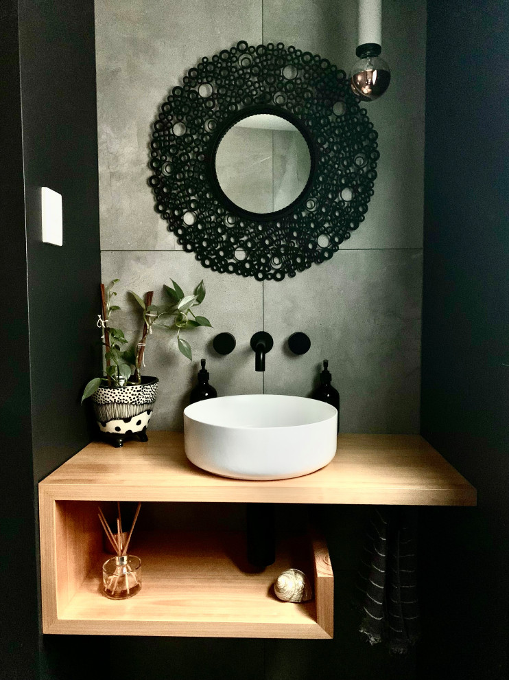 Idée de décoration pour un petit WC et toilettes bohème en bois clair avec WC à poser, un carrelage gris, des carreaux de céramique, un mur noir, un sol en carrelage de céramique, une vasque, un plan de toilette en bois, un sol gris et meuble-lavabo suspendu.