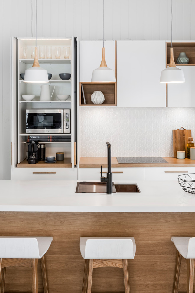 This is an example of a scandinavian galley kitchen in Brisbane with an undermount sink, flat-panel cabinets, white cabinets, quartz benchtops, white splashback, ceramic splashback, stainless steel appliances, ceramic floors and with island.