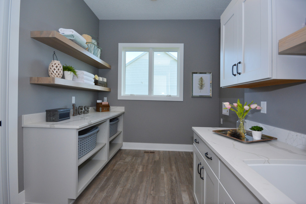 This is an example of a mid-sized modern galley dedicated laundry room in Other with an undermount sink, recessed-panel cabinets, white cabinets, quartz benchtops, grey walls, ceramic floors, a side-by-side washer and dryer, brown floor and white benchtop.
