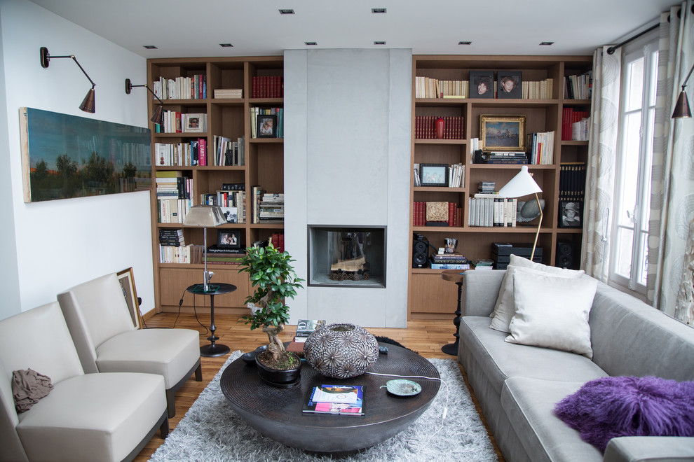 Photo of a mid-sized contemporary enclosed living room in Paris with a library, white walls, a standard fireplace, a concrete fireplace surround, no tv and medium hardwood floors.