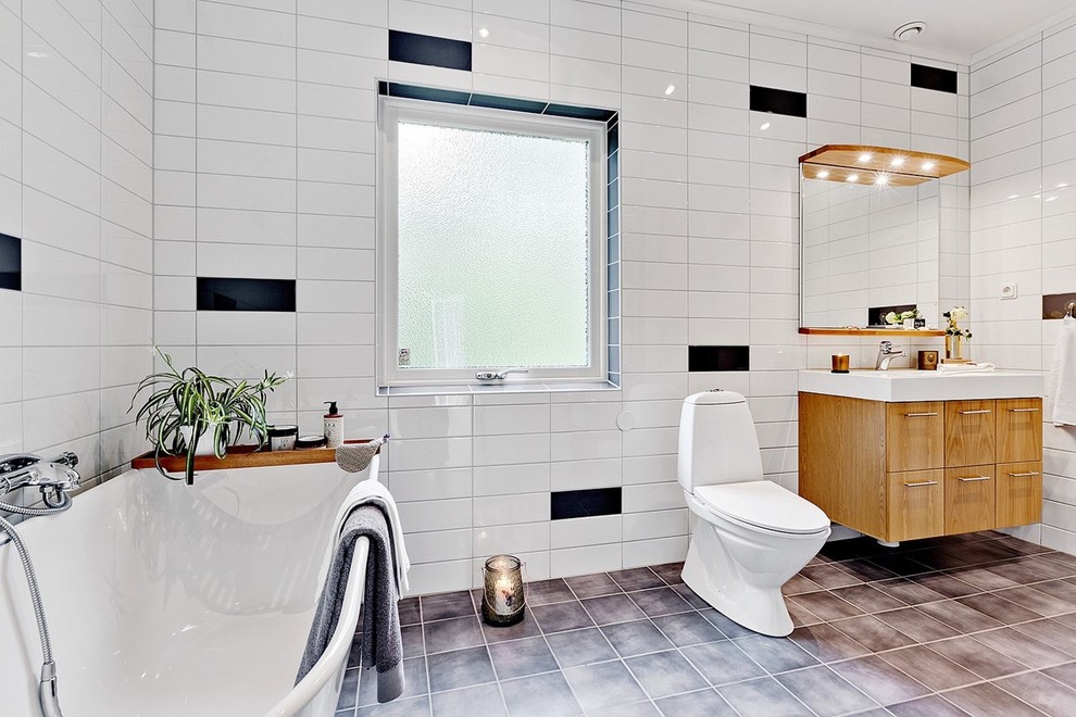 Mid-sized scandinavian bathroom in Stockholm with flat-panel cabinets, light wood cabinets, a claw-foot tub, a two-piece toilet, black tile, white tile, subway tile, white walls, a console sink and limestone floors.