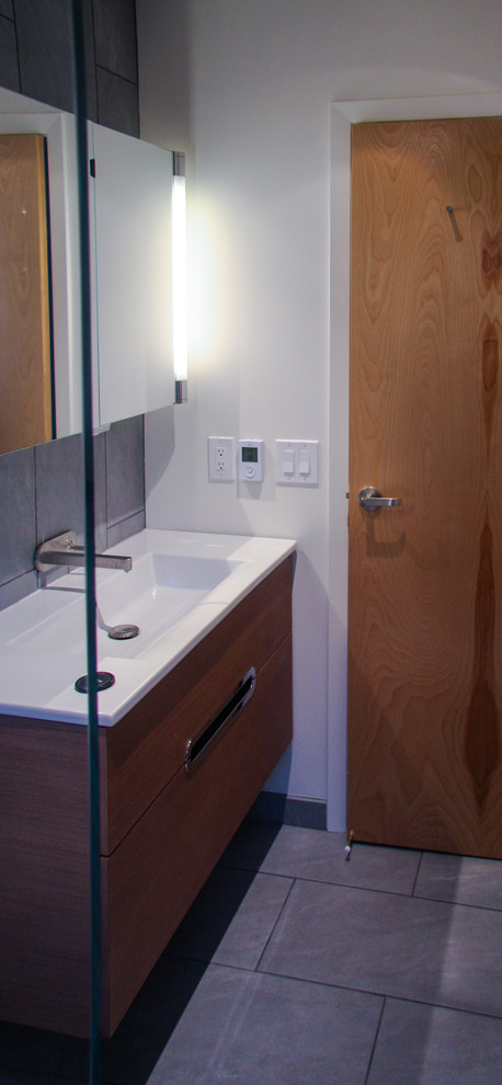 This is an example of a small contemporary 3/4 bathroom in San Francisco with flat-panel cabinets, medium wood cabinets, a curbless shower, a wall-mount toilet, gray tile, ceramic tile, white walls, ceramic floors and a wall-mount sink.
