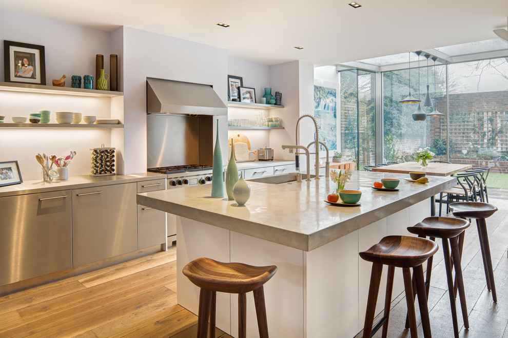 Contemporary open plan kitchen in London with an undermount sink, flat-panel cabinets, stainless steel cabinets, stainless steel appliances, medium hardwood floors, with island and concrete benchtops.