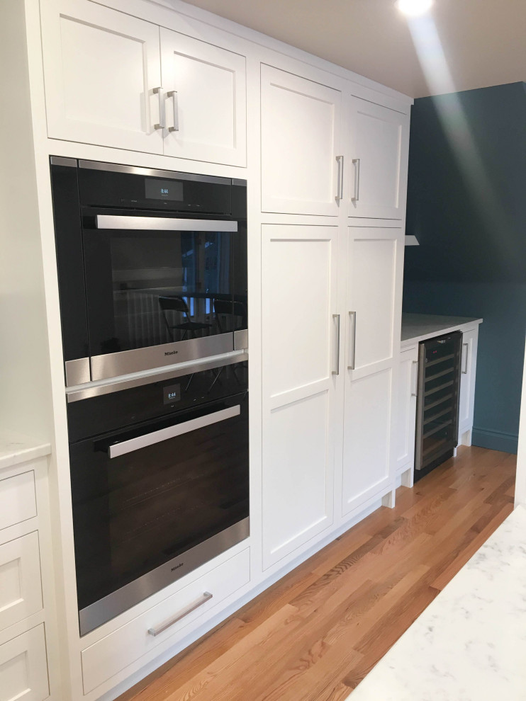 Large transitional u-shaped light wood floor and beige floor eat-in kitchen photo with a double-bowl sink, shaker cabinets, white cabinets, quartzite countertops, white backsplash, subway tile backsplash, stainless steel appliances, an island and white countertops