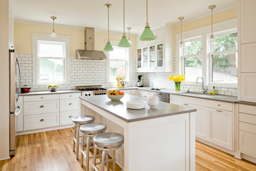 Inspiration for a mid-sized traditional u-shaped separate kitchen in Portland with an undermount sink, shaker cabinets, white cabinets, white splashback, subway tile splashback, stainless steel appliances, light hardwood floors, with island, concrete benchtops and brown floor.