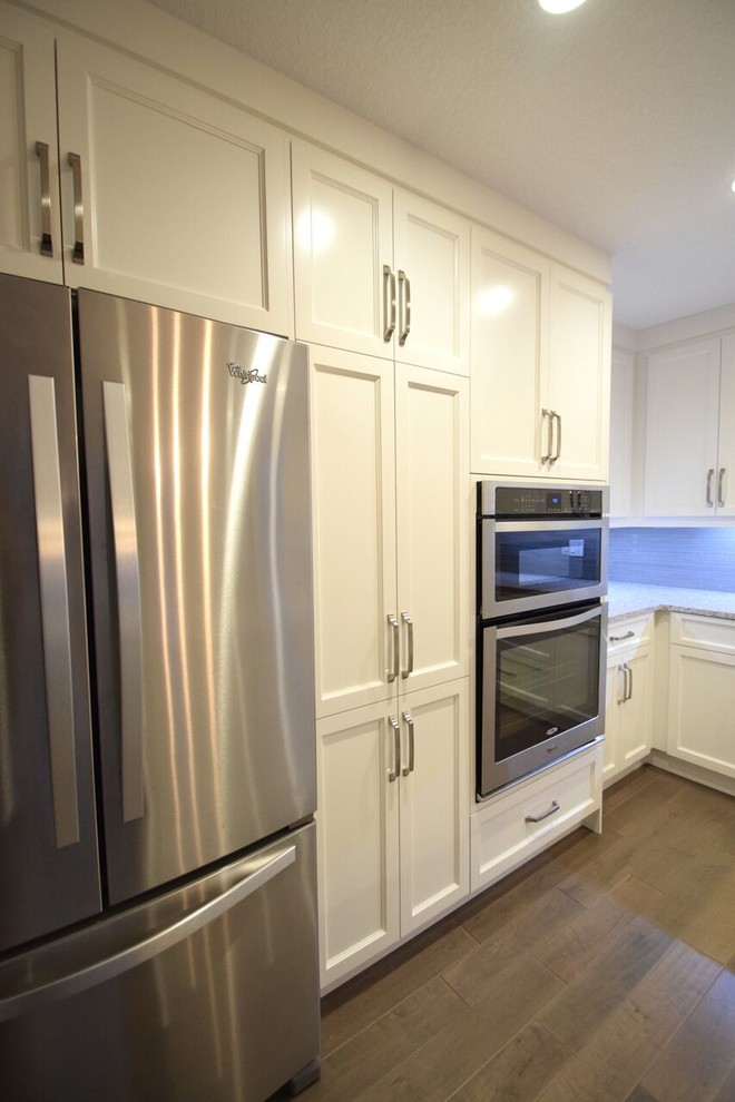Inspiration for a transitional l-shaped vinyl floor eat-in kitchen remodel in Edmonton with a double-bowl sink, shaker cabinets, white cabinets, quartz countertops, gray backsplash, glass tile backsplash, stainless steel appliances and an island