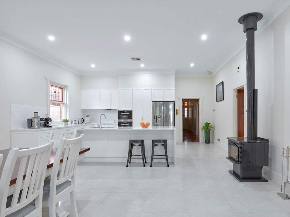 Design ideas for a large contemporary l-shaped open plan kitchen in Other with a double-bowl sink, shaker cabinets, white cabinets, quartz benchtops, white splashback, ceramic splashback, stainless steel appliances, porcelain floors, with island and white benchtop.