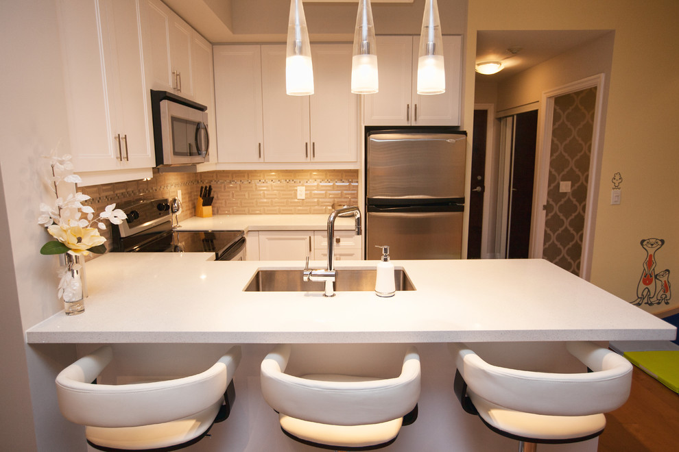This is an example of a small contemporary u-shaped open plan kitchen in Toronto with an undermount sink, recessed-panel cabinets, white cabinets, quartz benchtops, beige splashback, subway tile splashback, stainless steel appliances, light hardwood floors, a peninsula and beige floor.
