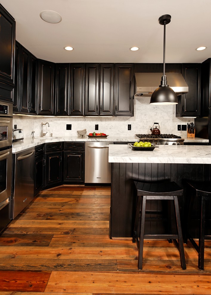 Photo of a large traditional u-shaped kitchen in DC Metro with stainless steel appliances, raised-panel cabinets, black cabinets, white splashback, stone slab splashback, brown floor, an undermount sink, quartzite benchtops, medium hardwood floors and with island.