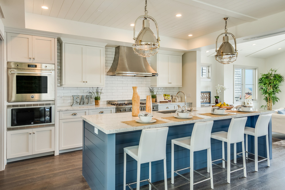 Beach style galley kitchen in Los Angeles with an undermount sink, shaker cabinets, white cabinets, white splashback, subway tile splashback, stainless steel appliances, dark hardwood floors and with island.