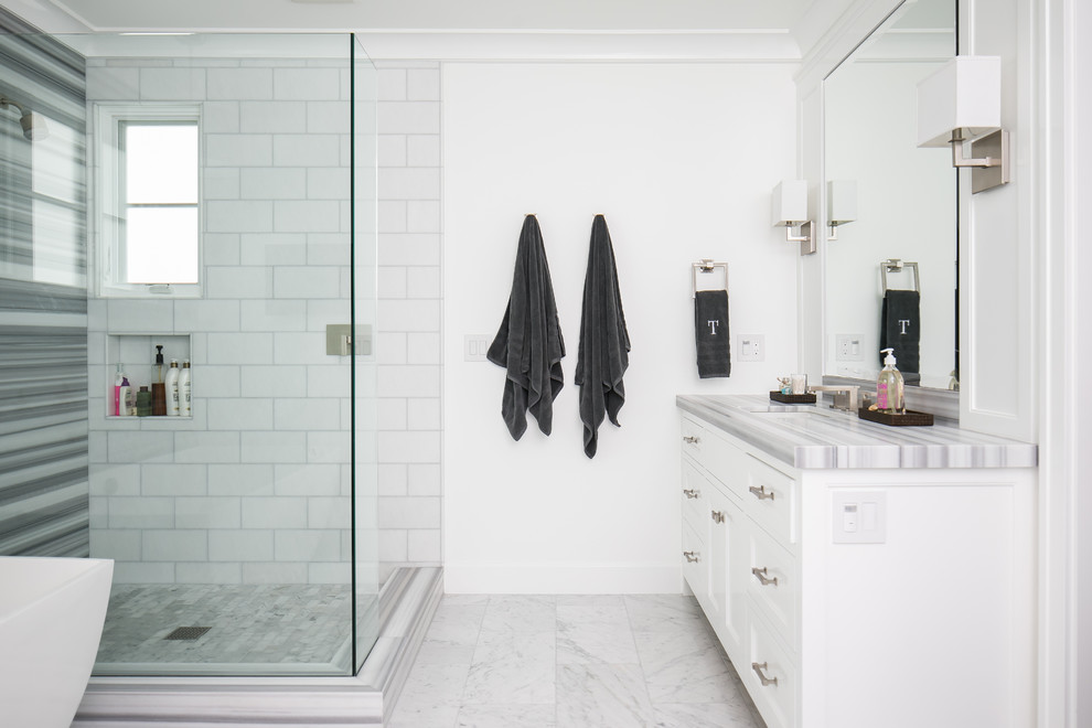 Photo of a mid-sized beach style master bathroom in Orange County with flat-panel cabinets, white cabinets, a freestanding tub, a corner shower, a one-piece toilet, white tile, ceramic tile, white walls, marble floors, an undermount sink, engineered quartz benchtops and grey benchtops.