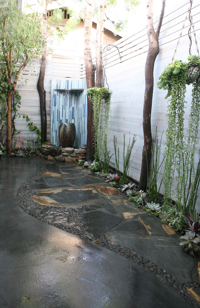 This is an example of a mid-sized transitional courtyard patio in Los Angeles with natural stone pavers, a water feature and no cover.