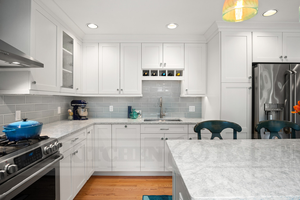Photo of a mid-sized beach style u-shaped eat-in kitchen in Providence with a double-bowl sink, shaker cabinets, white cabinets, quartz benchtops, blue splashback, porcelain splashback, stainless steel appliances, medium hardwood floors, with island, brown floor and multi-coloured benchtop.