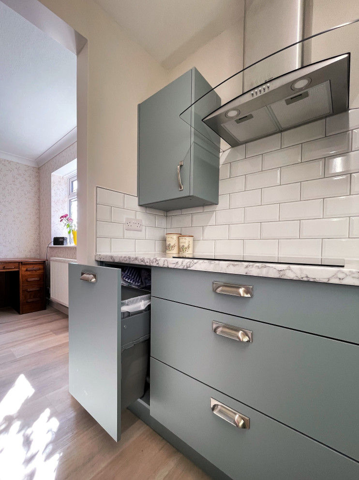 This is an example of a mid-sized modern galley separate kitchen in Other with a drop-in sink, flat-panel cabinets, green cabinets, laminate benchtops, white splashback, porcelain splashback, black appliances, light hardwood floors, no island, brown floor and white benchtop.