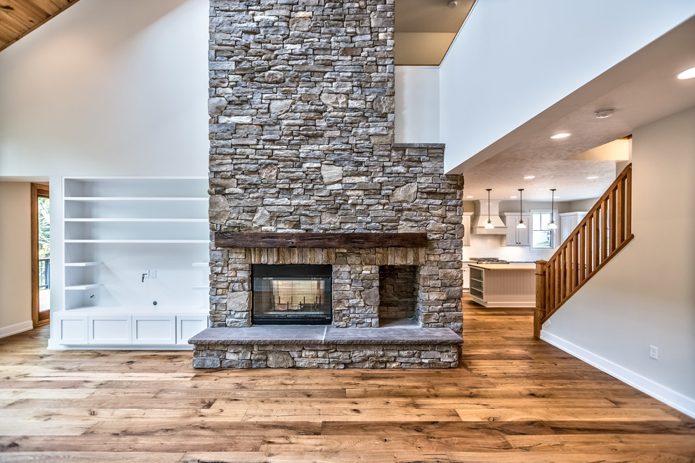 Large arts and crafts loft-style family room in Other with grey walls, medium hardwood floors, a two-sided fireplace, a stone fireplace surround, a built-in media wall and brown floor.