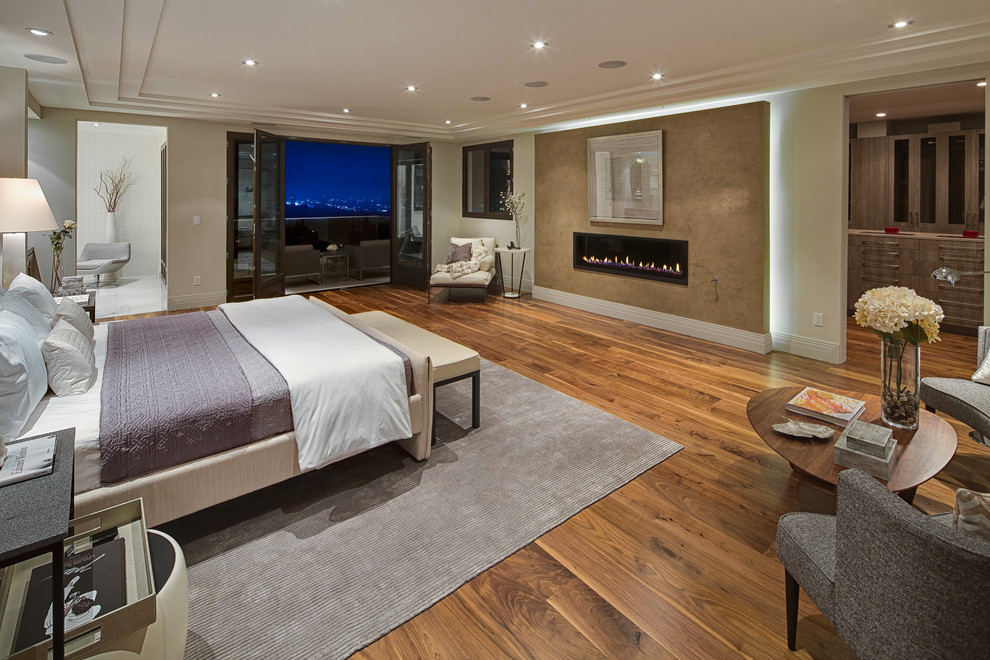 Large contemporary master bedroom in Los Angeles with beige walls, medium hardwood floors, a ribbon fireplace and a plaster fireplace surround.