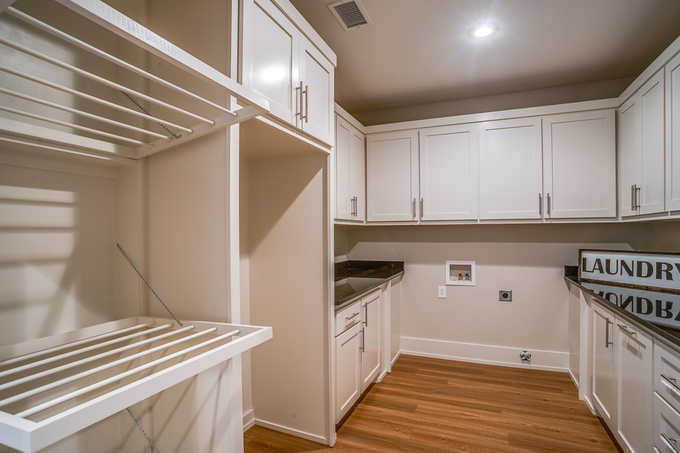 Photo of a mid-sized transitional laundry room in Austin with recessed-panel cabinets, white cabinets, granite benchtops, beige walls, light hardwood floors and beige floor.