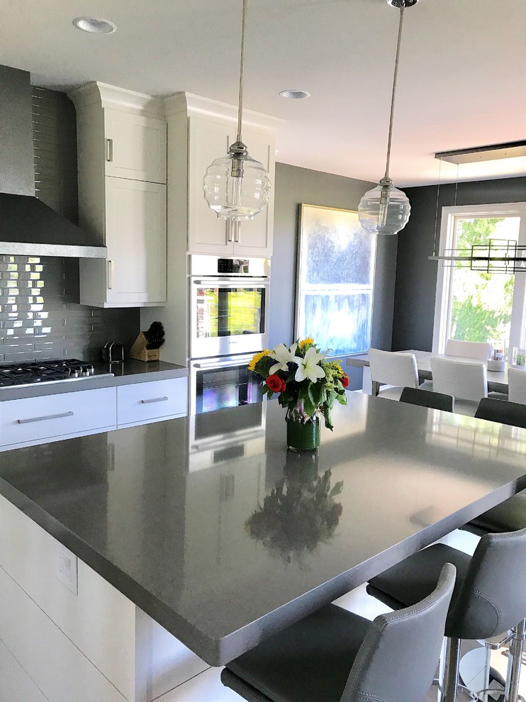 Eat-in kitchen - mid-sized transitional l-shaped light wood floor and gray floor eat-in kitchen idea with an undermount sink, recessed-panel cabinets, white cabinets, quartz countertops, gray backsplash, ceramic backsplash, stainless steel appliances and an island