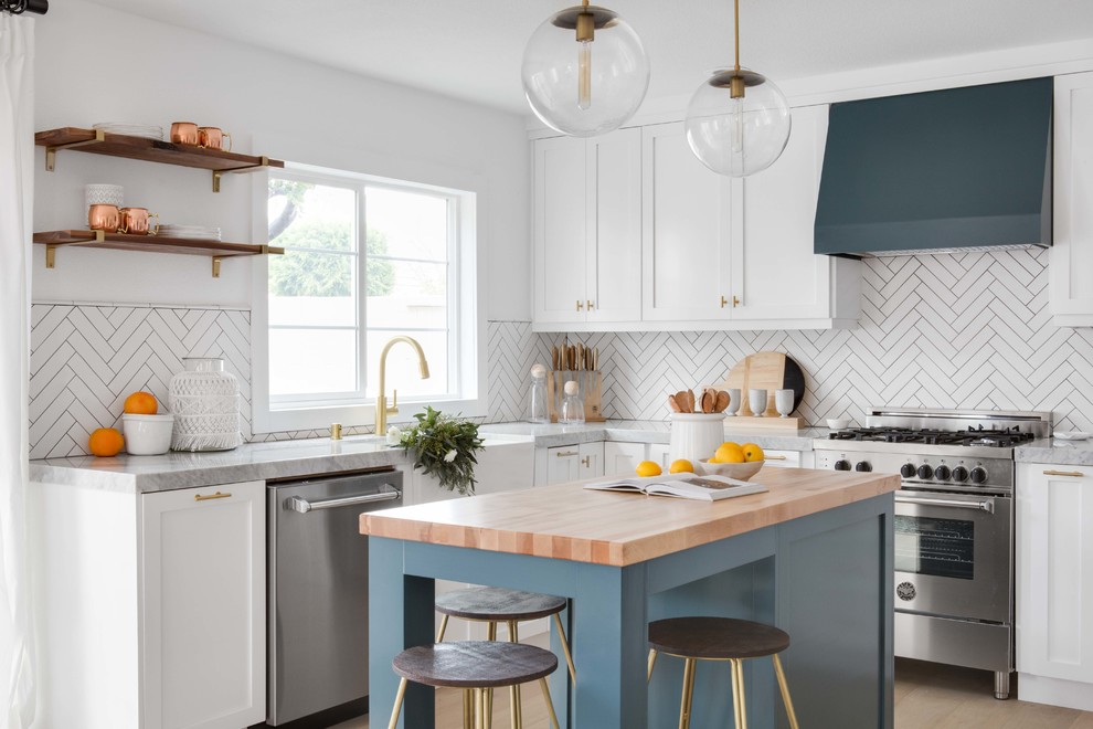 Inspiration for a mid-sized eclectic open plan kitchen in Orange County with a farmhouse sink, white cabinets, marble benchtops, white splashback, ceramic splashback, light hardwood floors and with island.