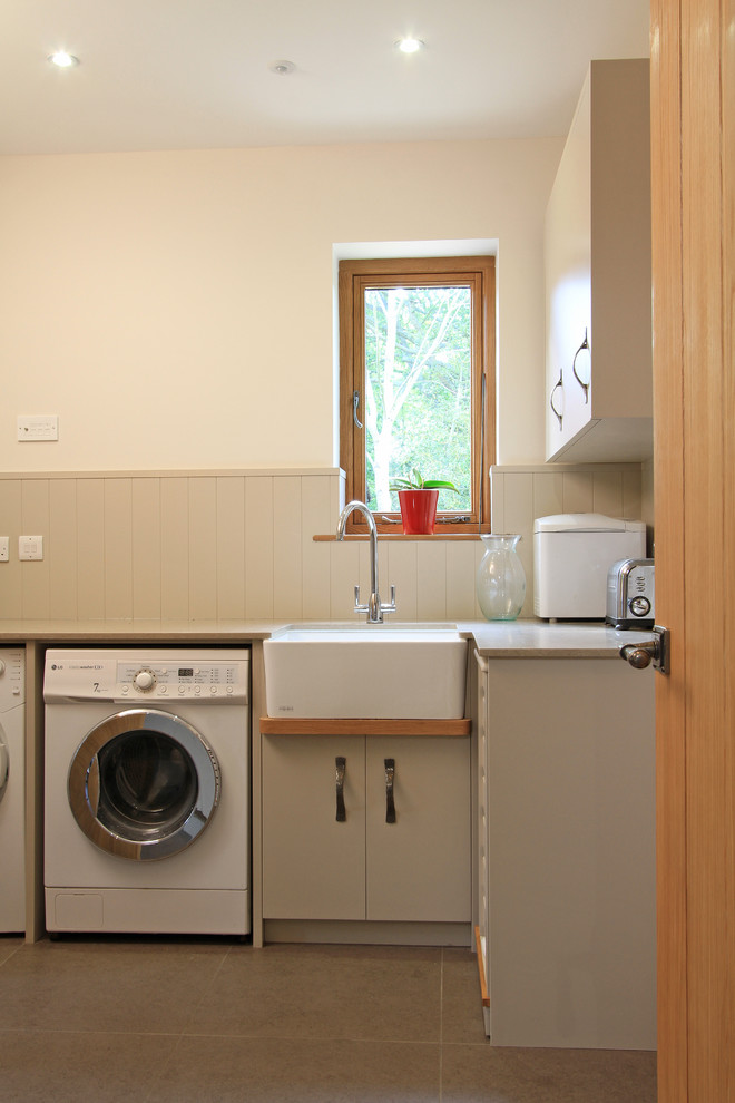 Inspiration for a large contemporary l-shaped utility room in Hampshire with an undermount sink, flat-panel cabinets, beige cabinets, quartz benchtops, white walls, porcelain floors and a side-by-side washer and dryer.